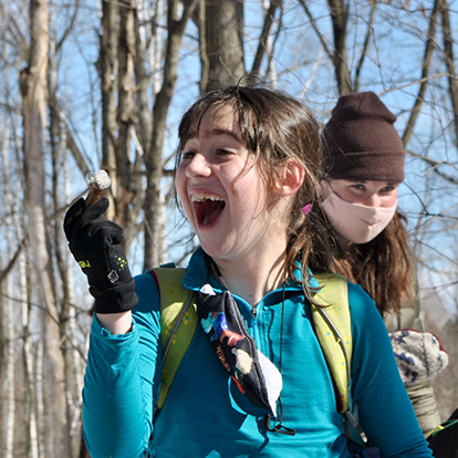 girl with dark hair looking to the left and smiling wide. other people in the background