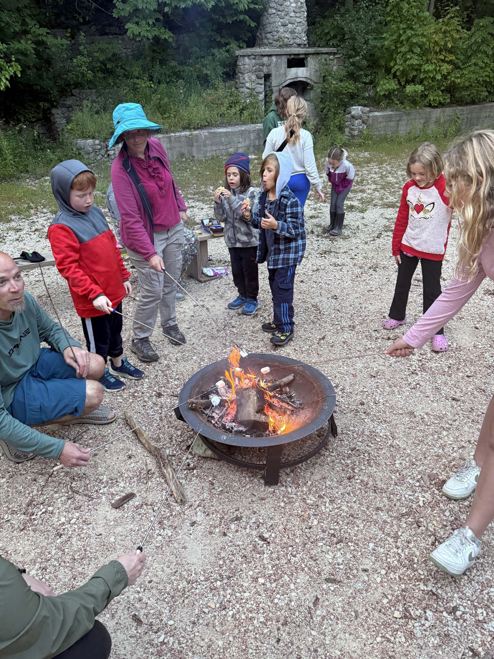 a group of families roasting marshmallows around a campfire at Riveredge