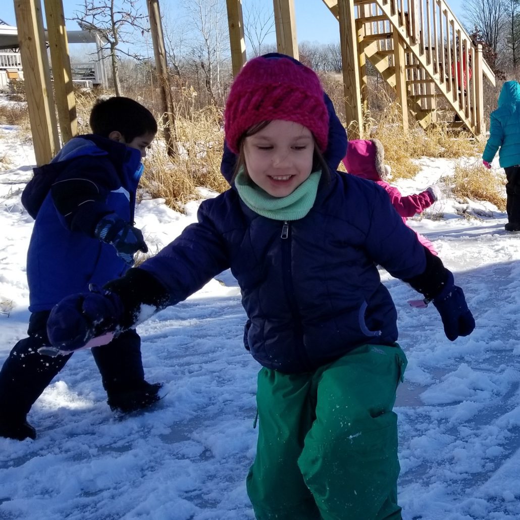 young children in winter gear happil playing at the Riveredge natural play area in winter