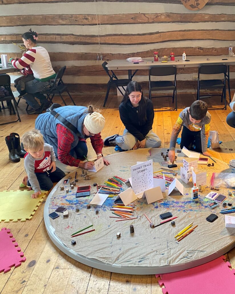 a small group of kids and parents gather around a mat on the floor and make crafts with paper