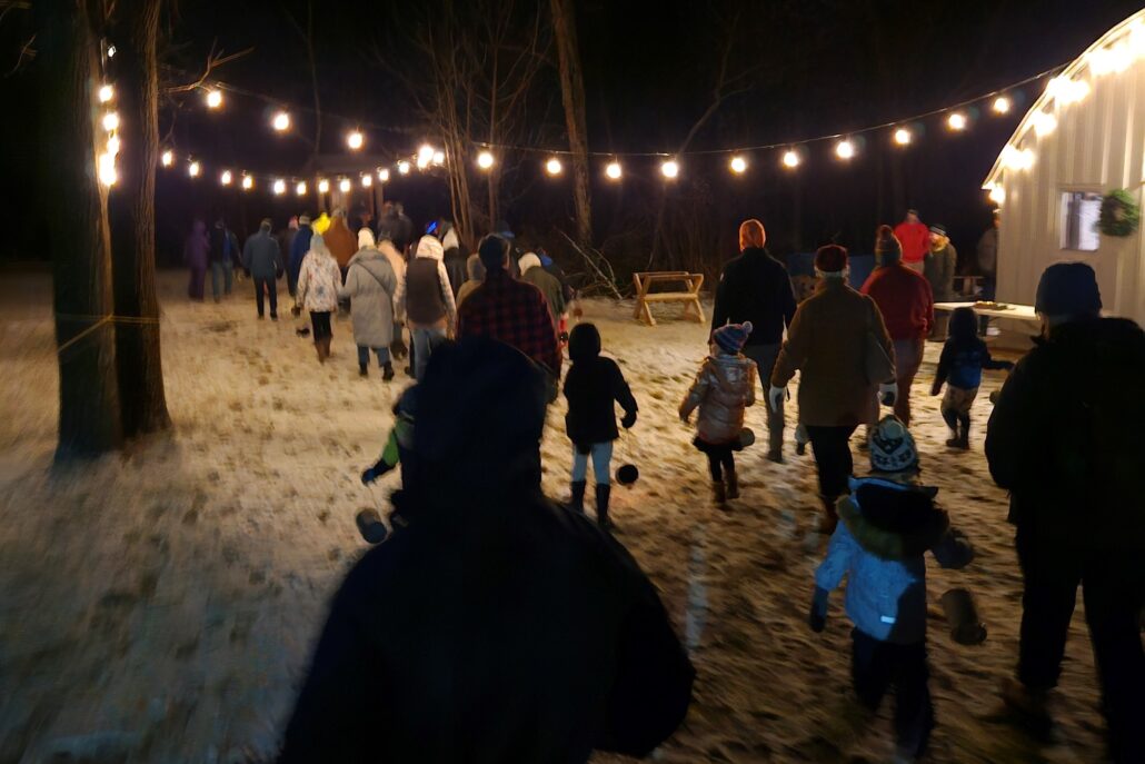 a group of families outside in winter at night holding lanterns while searching for the Yule Log at Riveredge