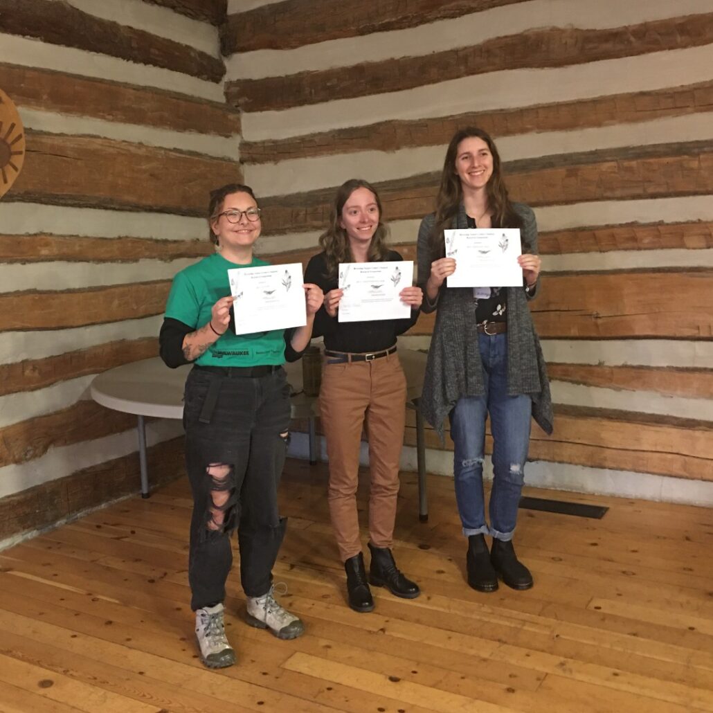 3 students hold up their winners certificates and smile at the camera