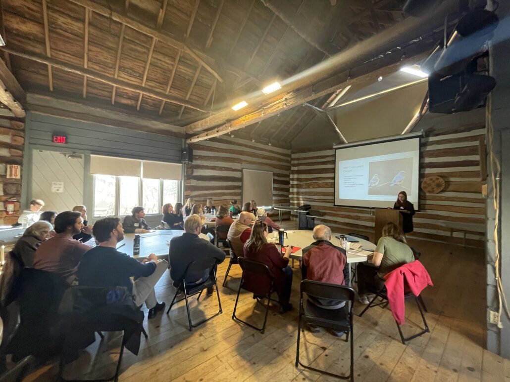 a student presents their research with a slide presentation to an audience in the Riveredge Barn