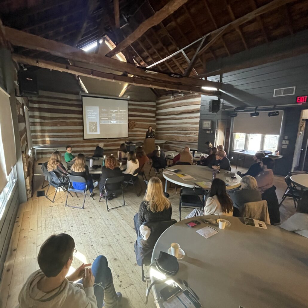 a student presents their research with a slide presentation to an audience in the Riveredge Barn