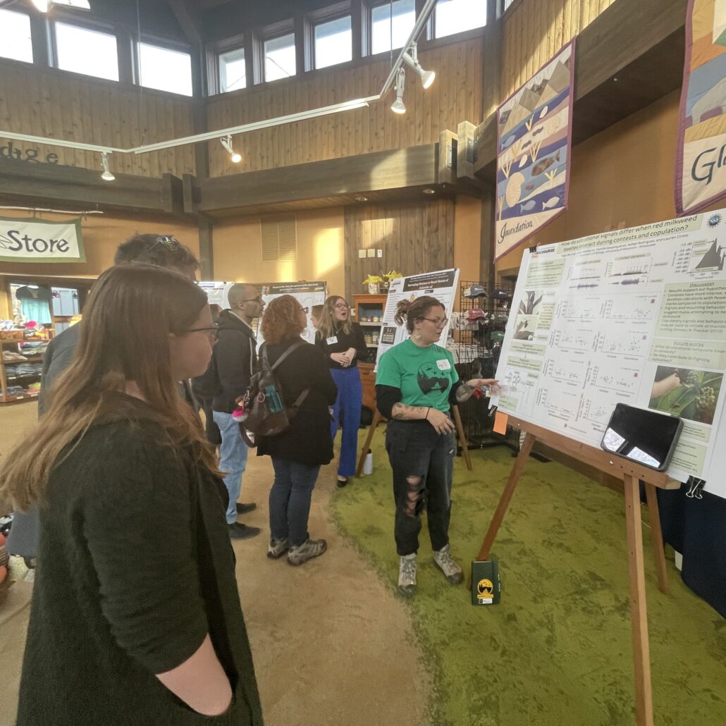 a student presents their research poster to a small group of people at the Riveredge Research Symposium