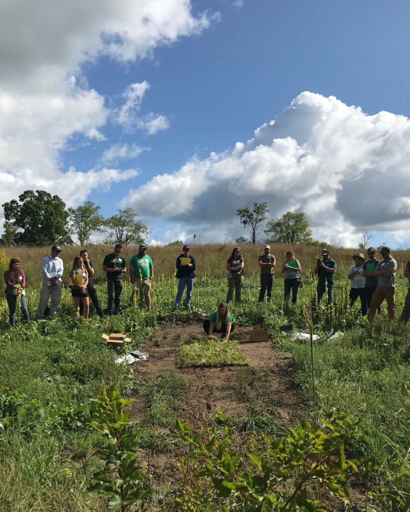 a group of adults gather around a small patch of land being studied