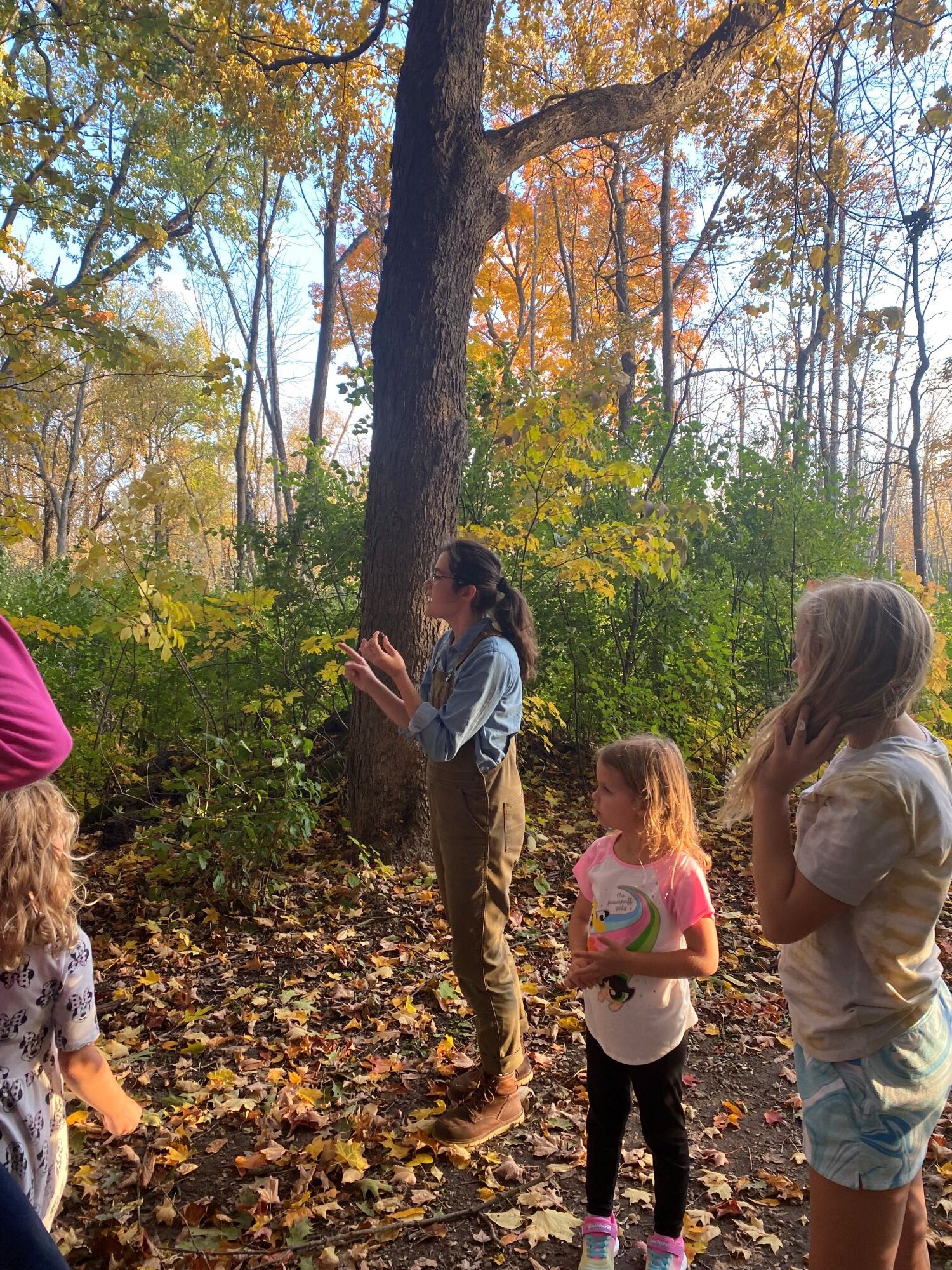 a few young kids listen to a Riveredge educator talk in an autumn forest