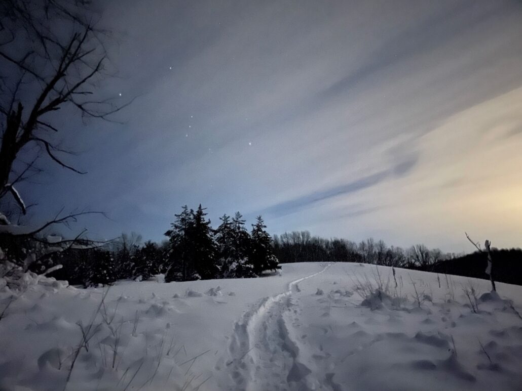 scenic winter landscape with snow on the trail, evergreen trees in the background, and wispy clouds in the sky