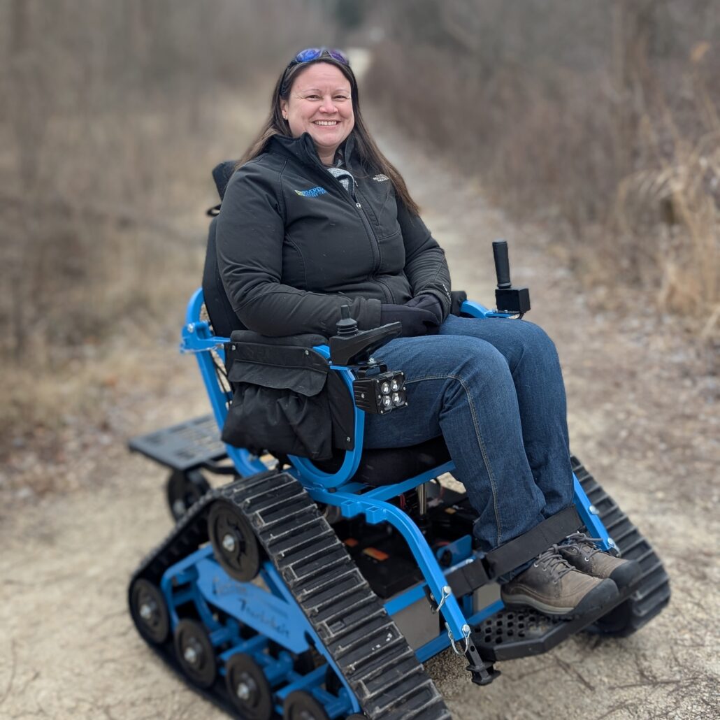 a woman sitting in a bright blue trackchair on a gravel Riveredge trail in winter