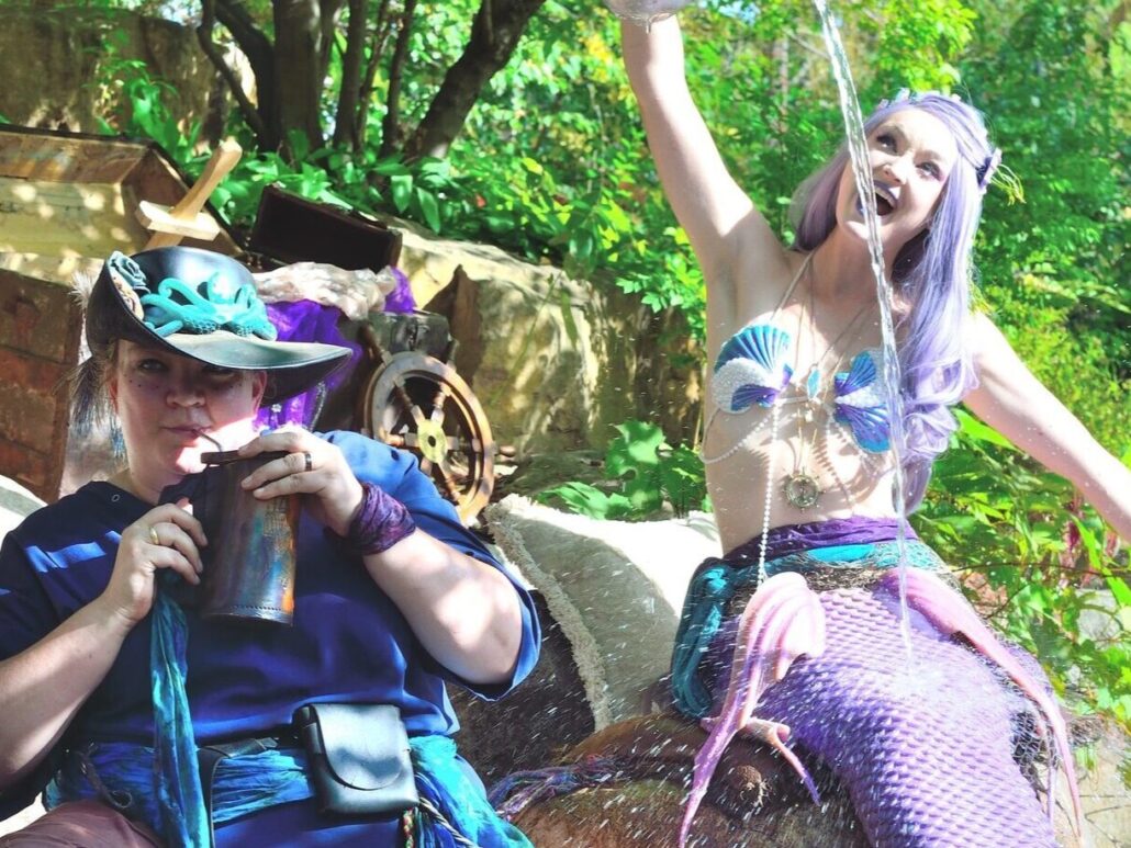 a woman dressed as a mermaid sitting on a rock on a sunny day with a whimsical friend sitting next to her