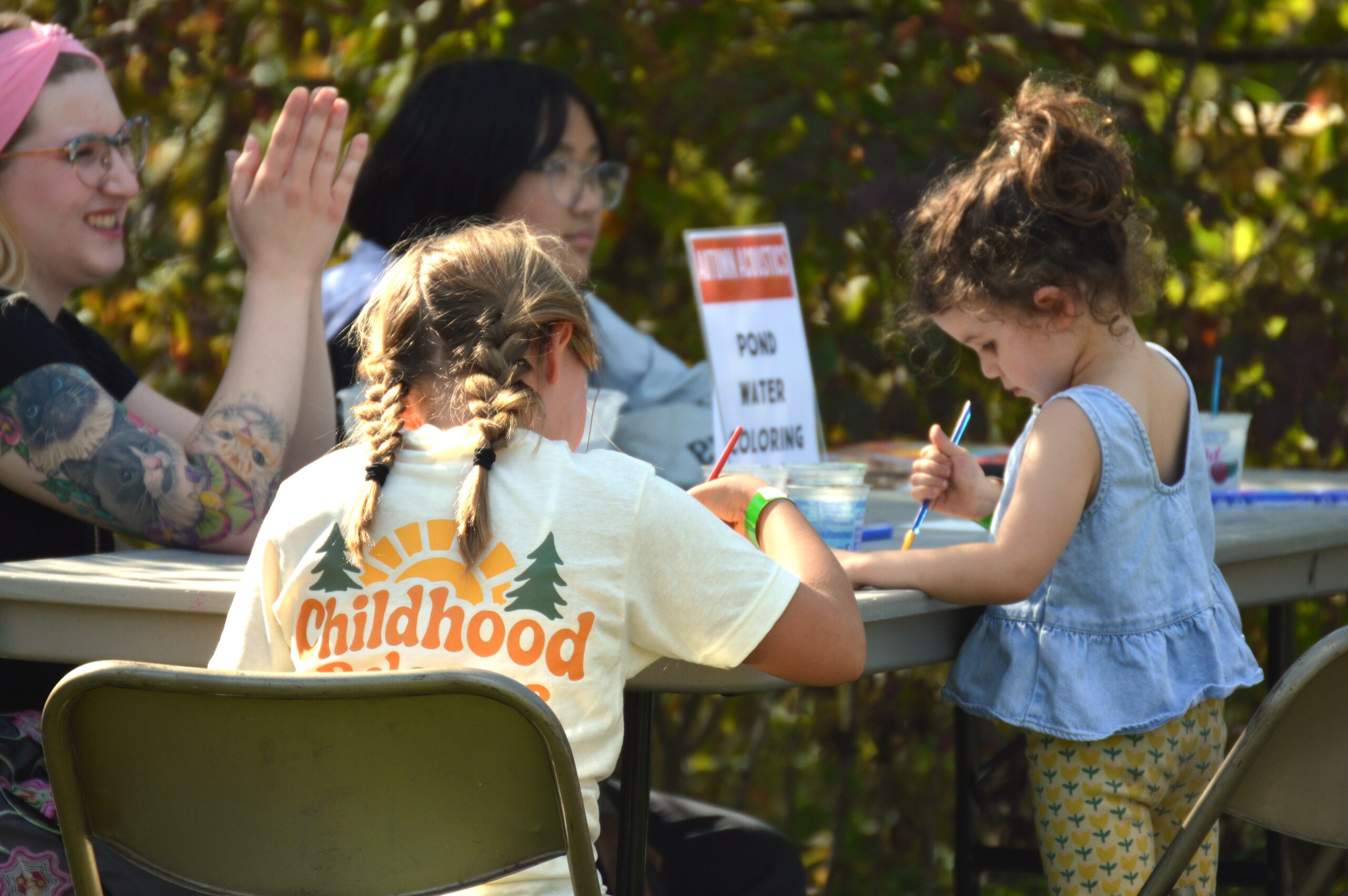 2 kids painting with water colors at a table with 2 adults supervising