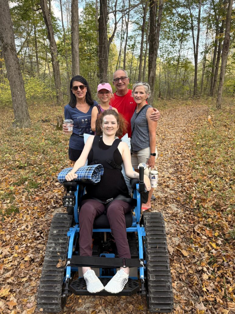 a woman sitting in the Riveredge trackchair with 4 other adults hiking on the trail next to her